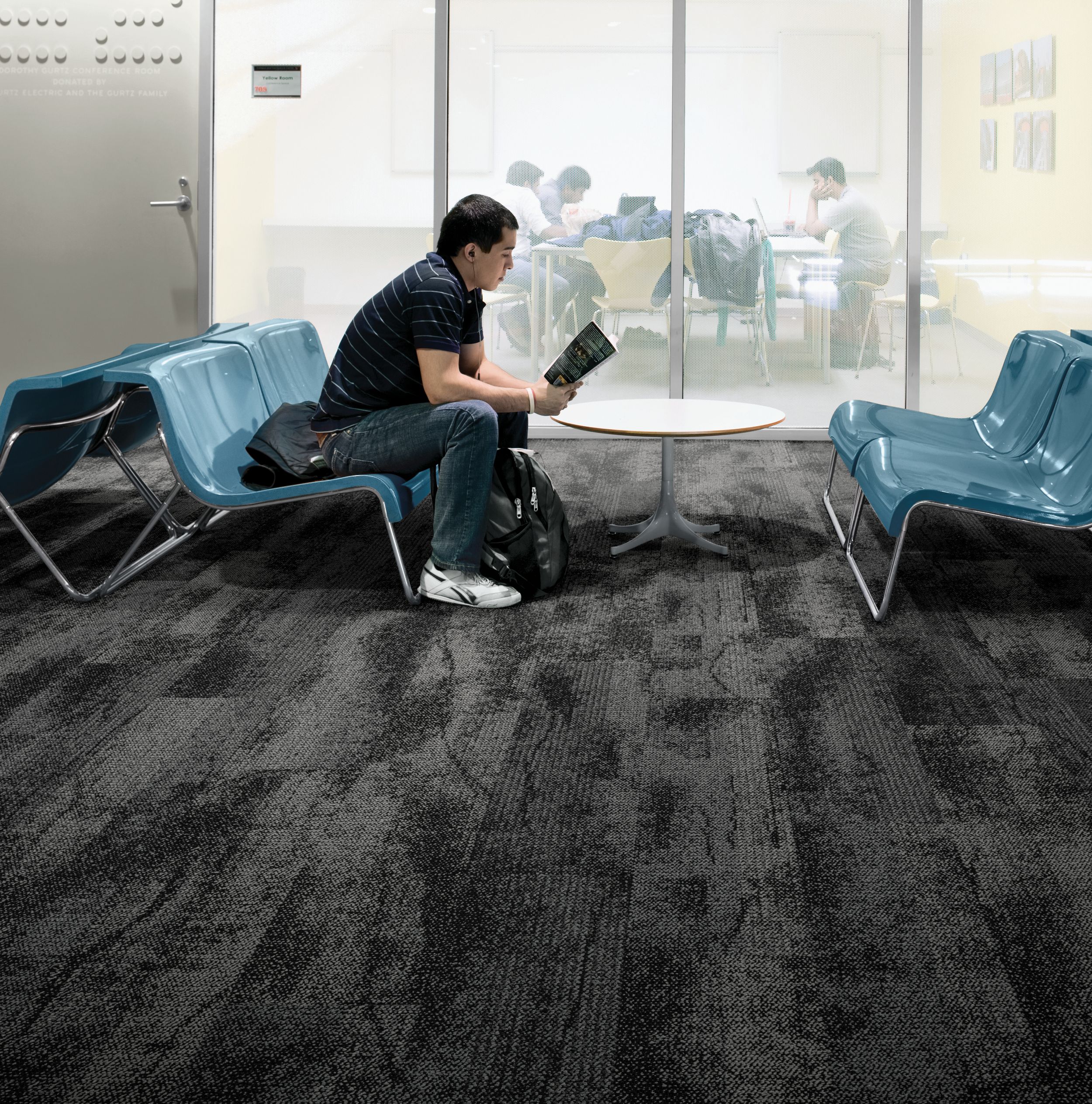 Interface Neighborhood Smooth plank carpet tile in public education space with man reading a book on blue chair imagen número 2